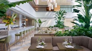 A modern restaurant with a bar, seating areas, and indoor plants.
