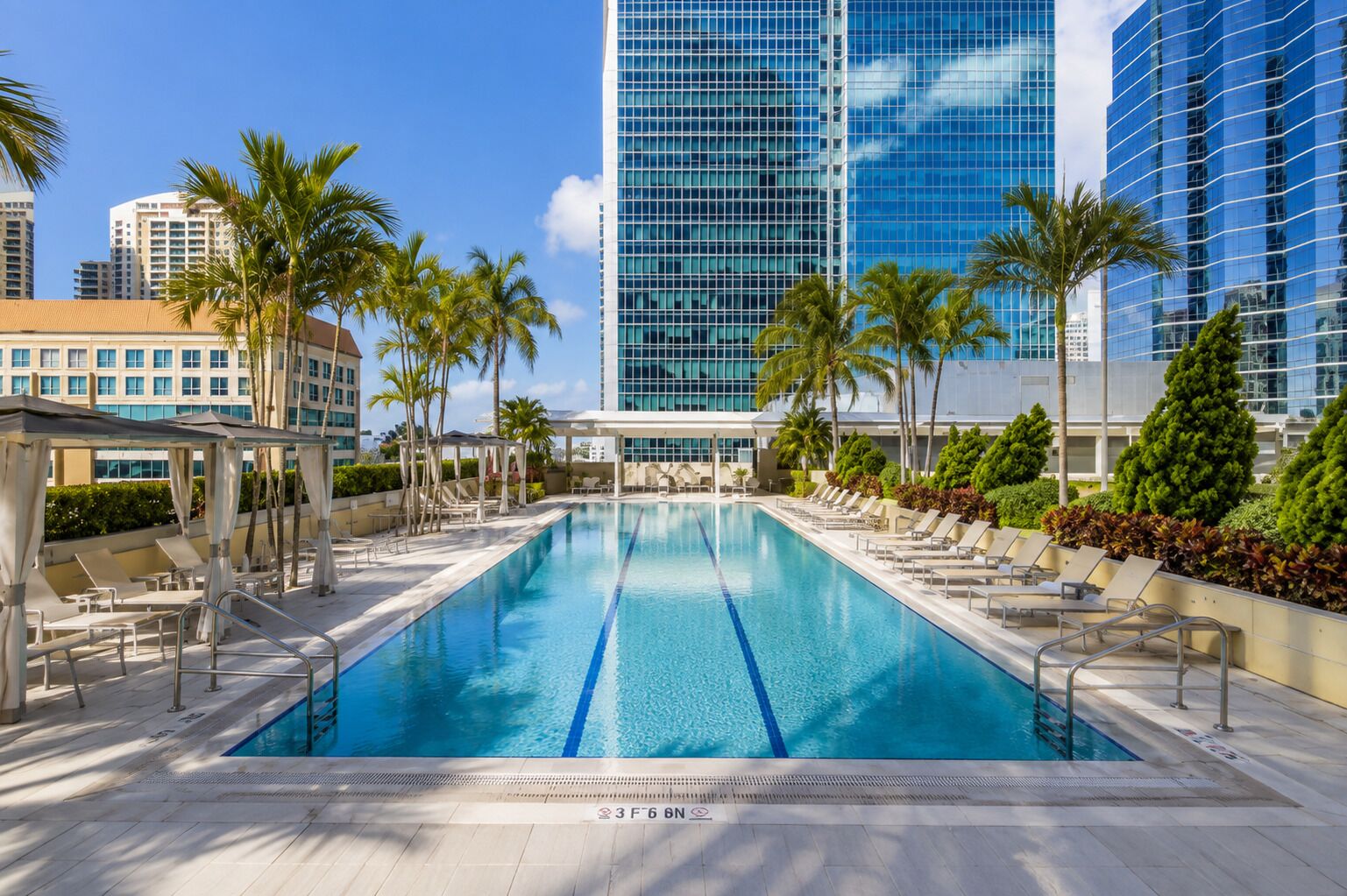 Una piscina con sillas de descanso y palmeras, rodeada de edificios modernos.