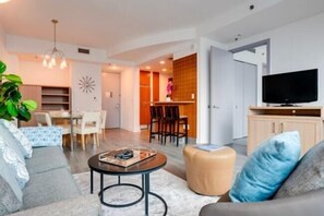 Una sala de estar moderna con un sofá, una mesita de centro y un televisor. Hay un comedor con sillas y una mesa.