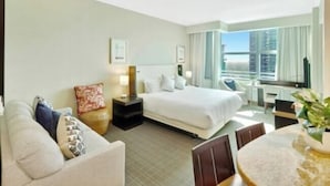 A hotel room with a bed, a desk, a chair, a TV, and a window with a city view.