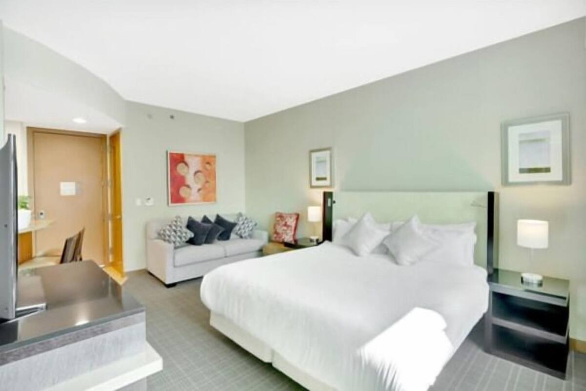 A hotel room with a bed, a sofa, a desk, and a TV.
