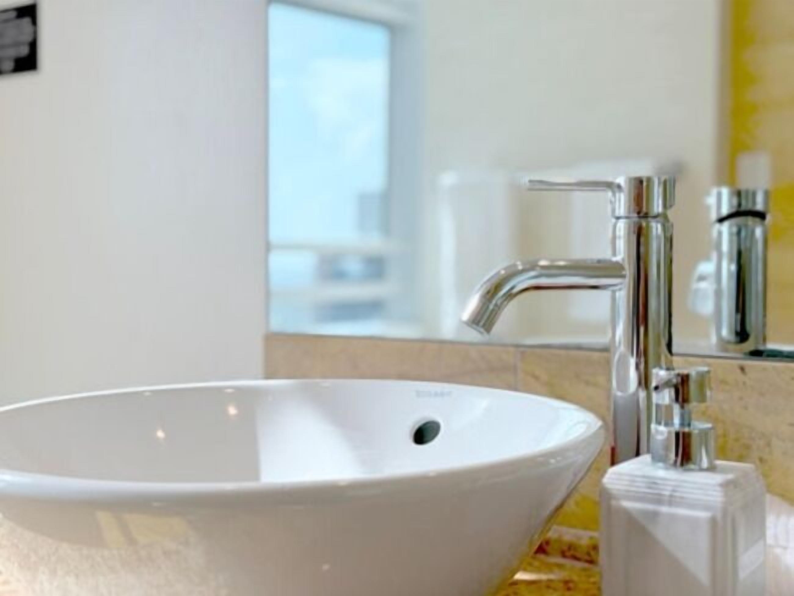 Een moderne badkamer met een witte wastafel, een chromen kraan en een kleine witte zeepdispenser op het aanrecht.