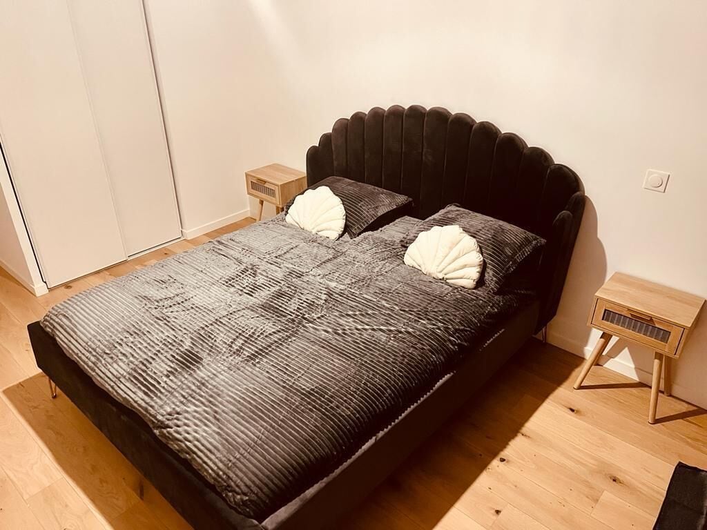 Een bed met een donker hoofdbord, twee kussens en een gebreid sprei. Er staan twee nachtkastjes met lampen.