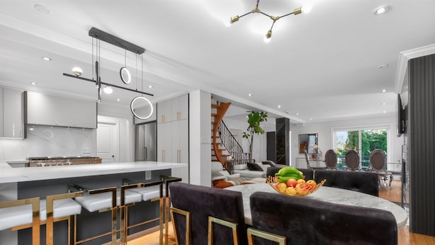 A modern kitchen with a marble countertop, bar stools, and a fruit bowl on the island. - Luxury Executive Home Near Airport & Downtown (Toronto)