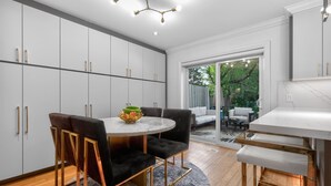 A modern kitchen with white cabinets, a marble countertop, and a dining area with a round table and chairs. - Luxury Executive Home Near Airport & Downtown (Toronto)