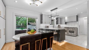 A modern kitchen with a central island, a dining area with a marble table, and a view of the outdoors. - Luxury Executive Home Near Airport & Downtown (Toronto)