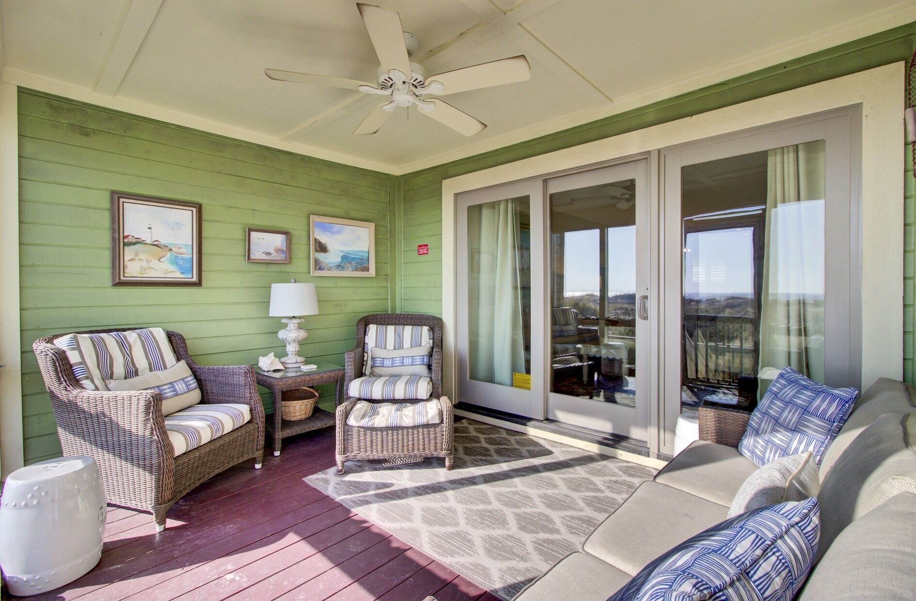 A covered porch with wicker furniture, a ceiling fan, and a view through glass doors.