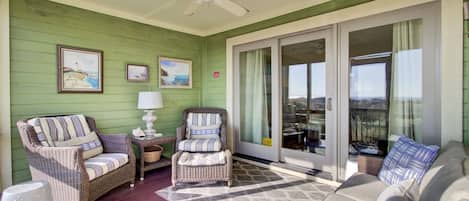 A covered porch with wicker furniture, a ceiling fan, and a view through glass doors.