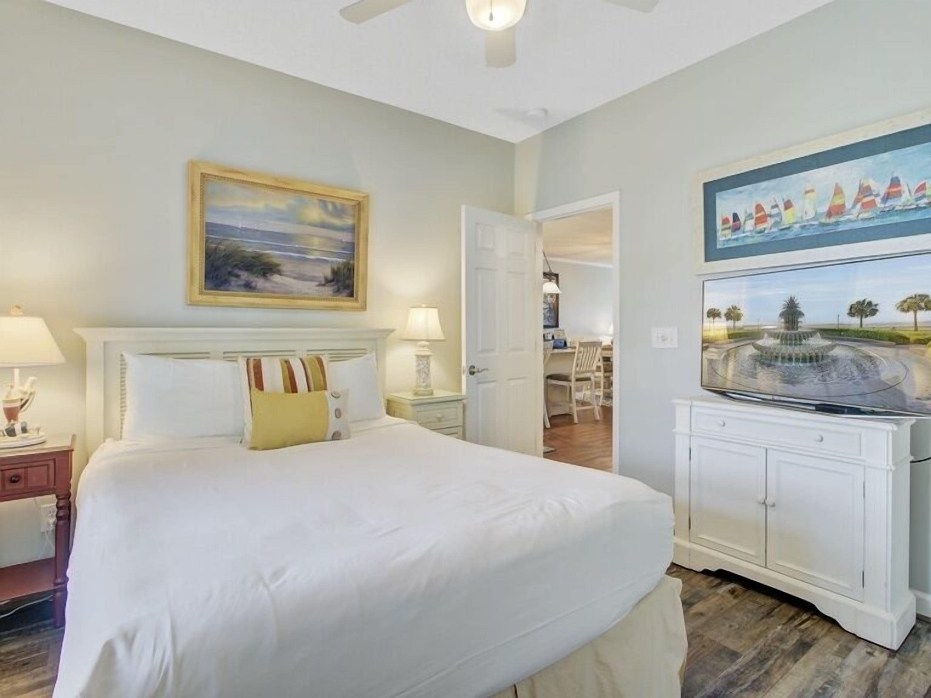 A bedroom with a large bed, bedside tables, a TV, and artwork on the walls.