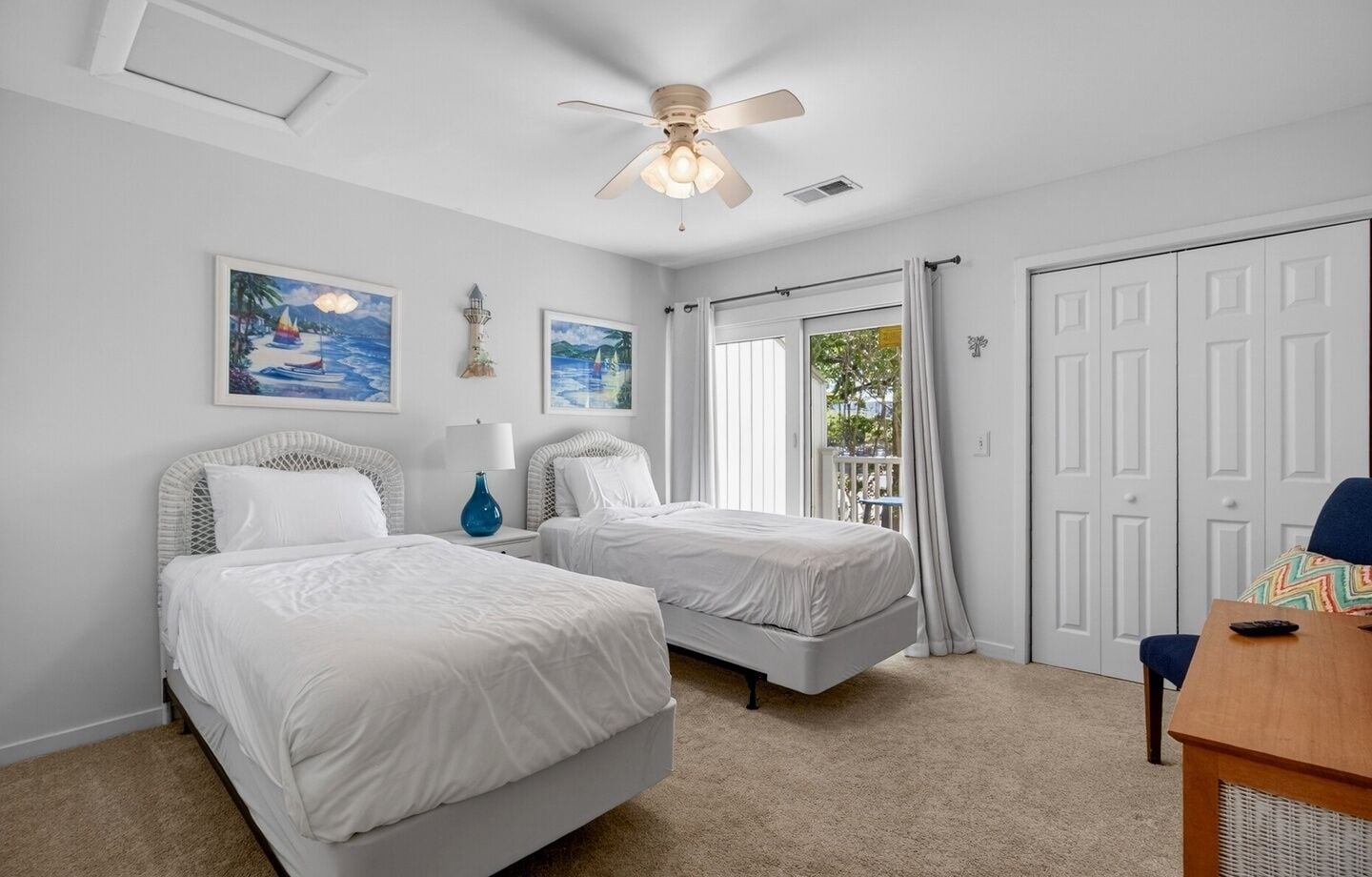A bedroom with two beds, a ceiling fan, a desk, and a window with curtains.