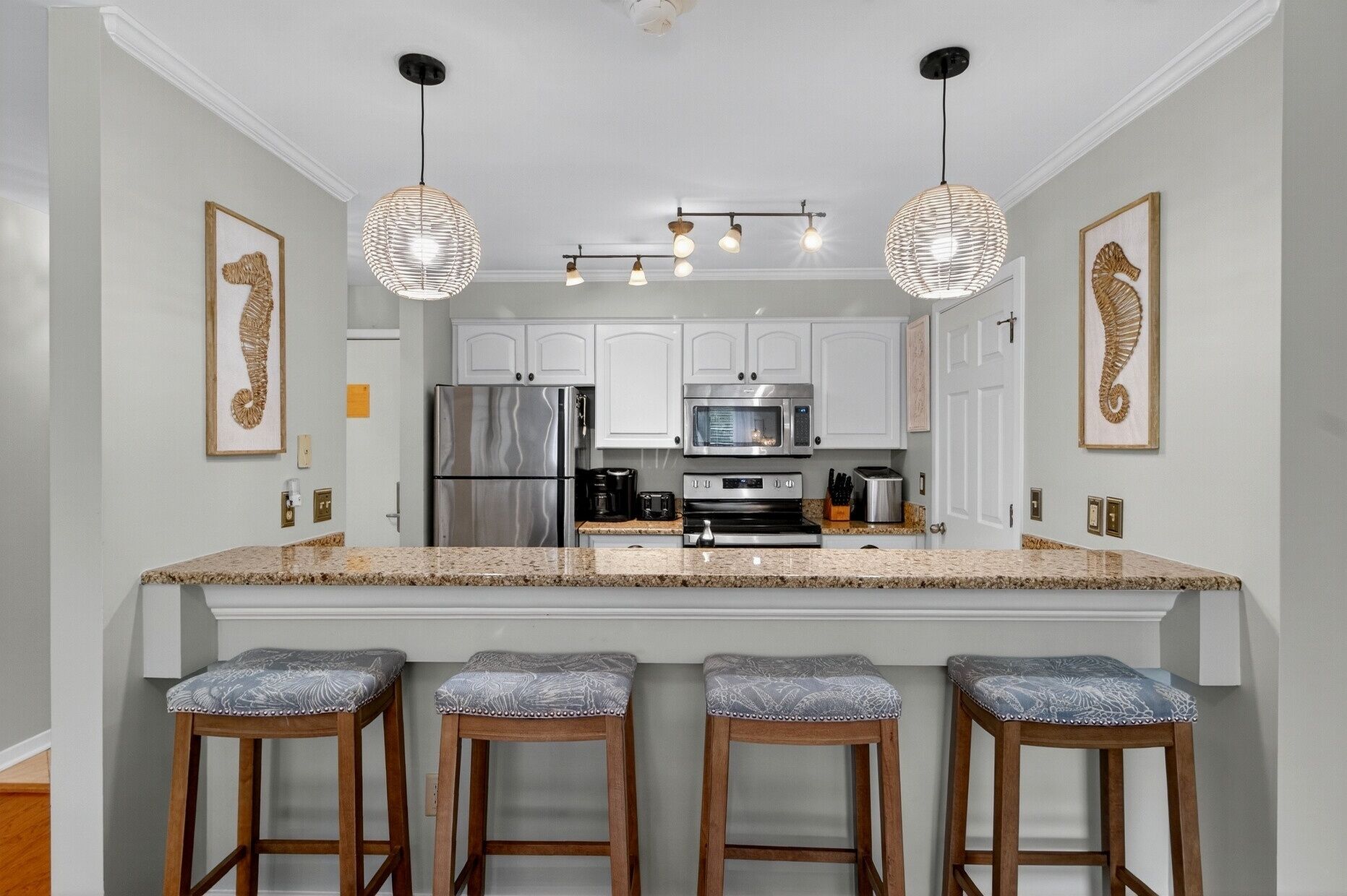 A kitchen with white cabinets, stainless steel appliances, and a central island with bar stools.