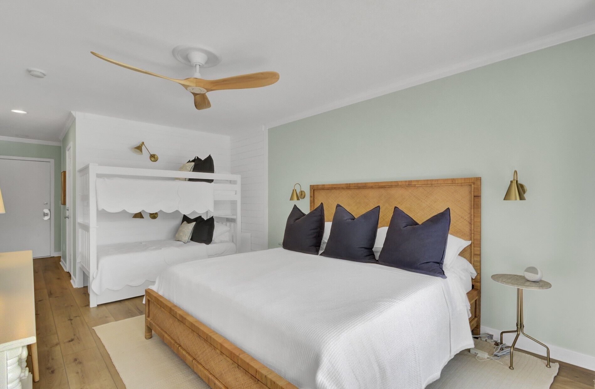A bedroom with a bed, a ceiling fan, a white wardrobe, and a small table.