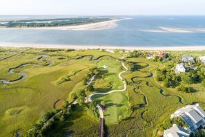 An aerial view of a golf course with winding paths, a large body of water, and residential buildings.