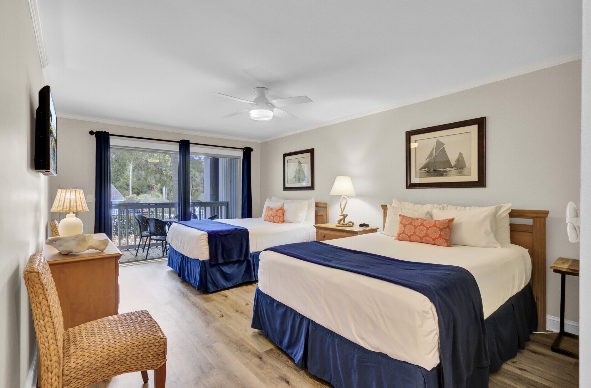 A hotel room with two beds, a balcony, a ceiling fan, and a large window.