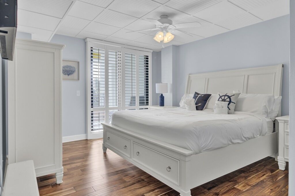 A bedroom with a white bed, a nightstand, a dresser, and a ceiling fan.