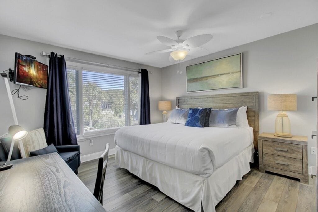 A bedroom with a bed, a desk, a chair, a ceiling fan, and a window with curtains.