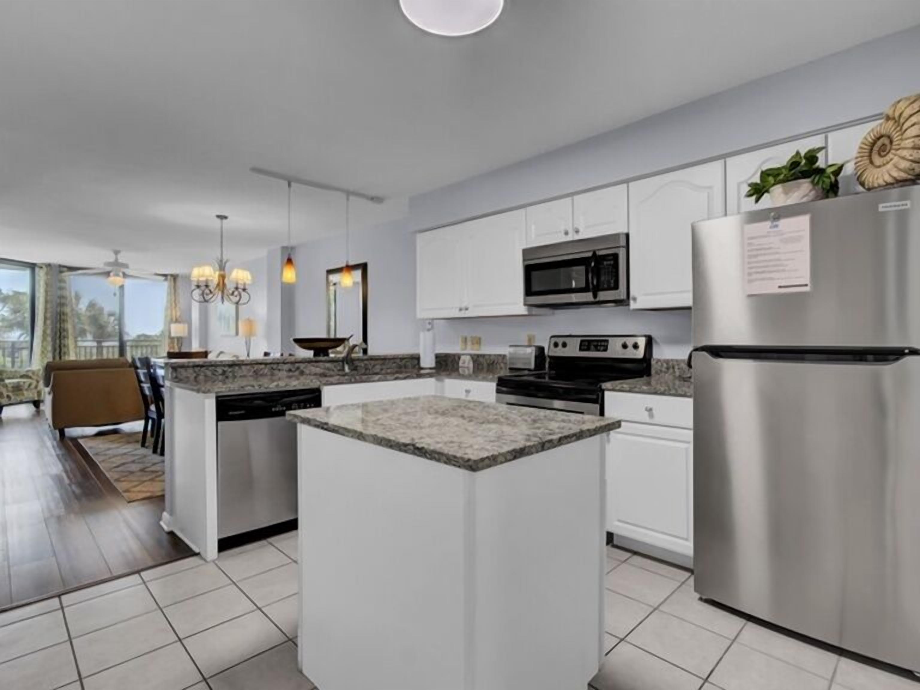 A modern kitchen with white cabinets, stainless steel appliances, a granite countertop island, and a dining area with a view.