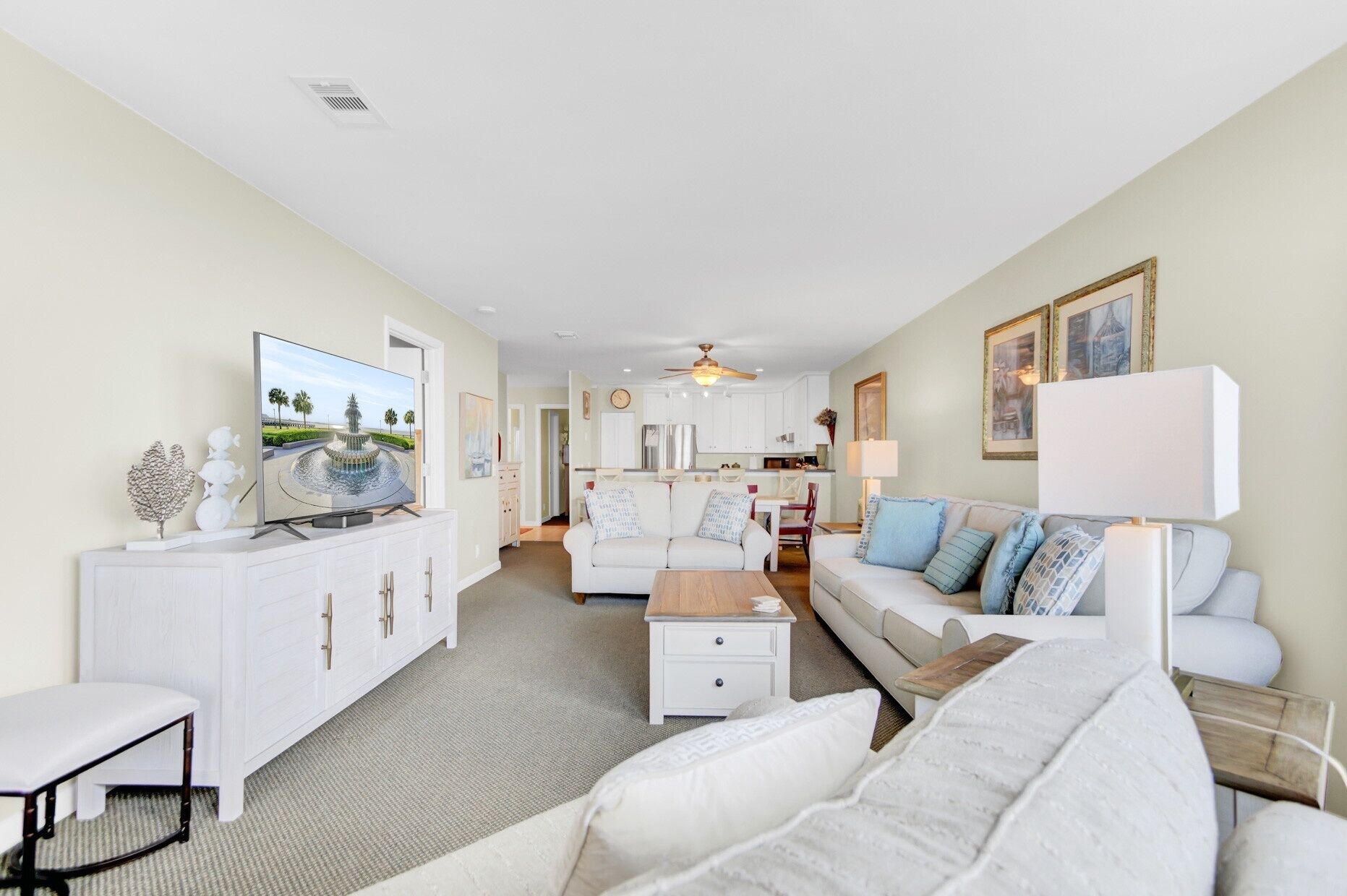 A spacious living room with a flat-screen TV, a white sofa, a coffee table, and a dining area in the background.