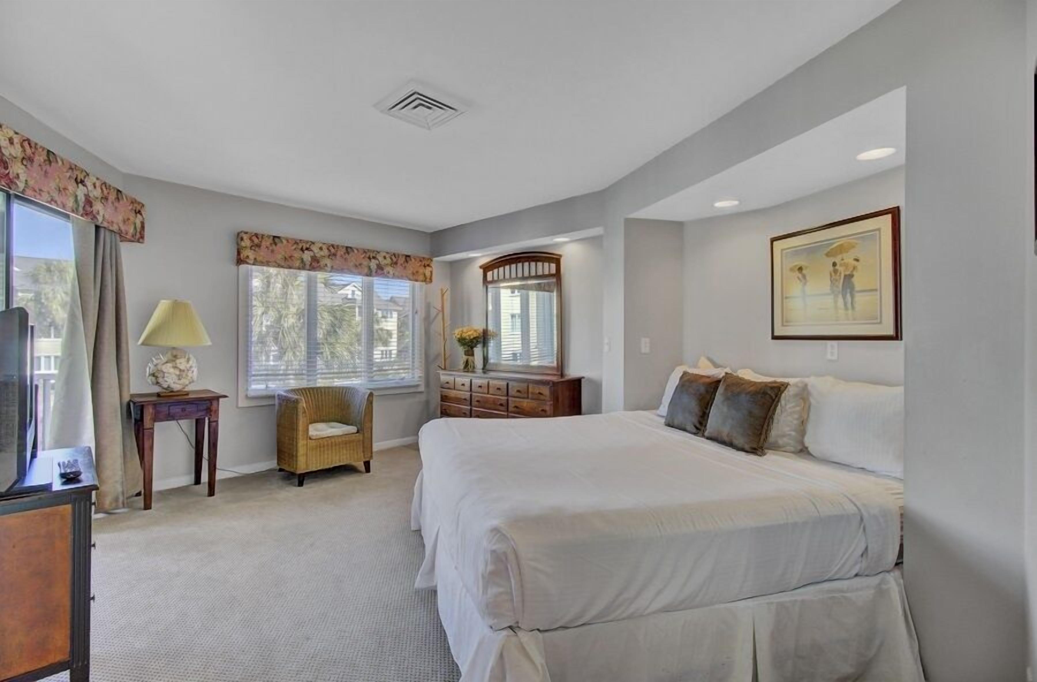 A bedroom with a large bed, a dresser, a chair, and a window with curtains.