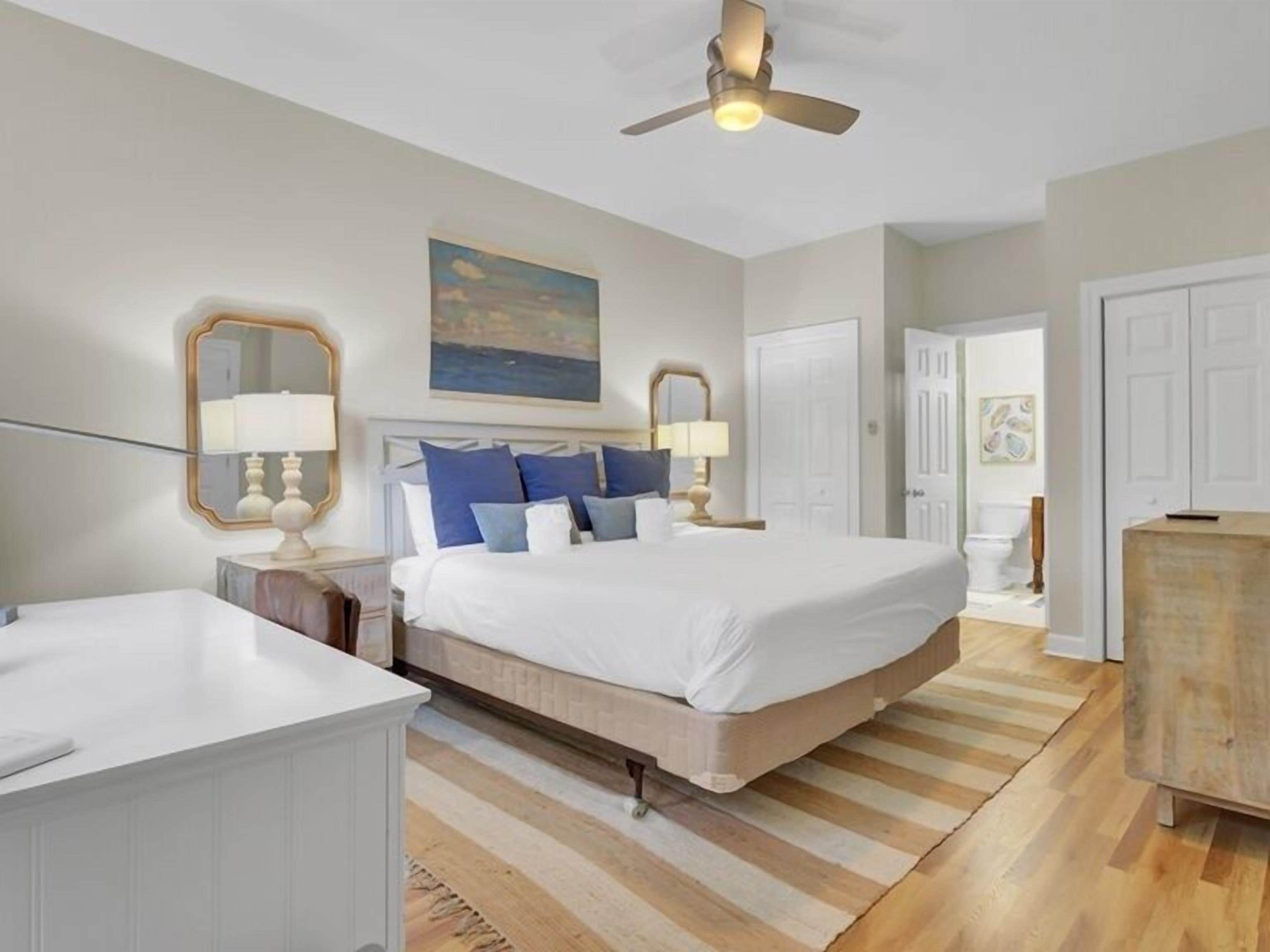 A bedroom with a large bed, bedside tables, a ceiling fan, and a view of the bathroom.