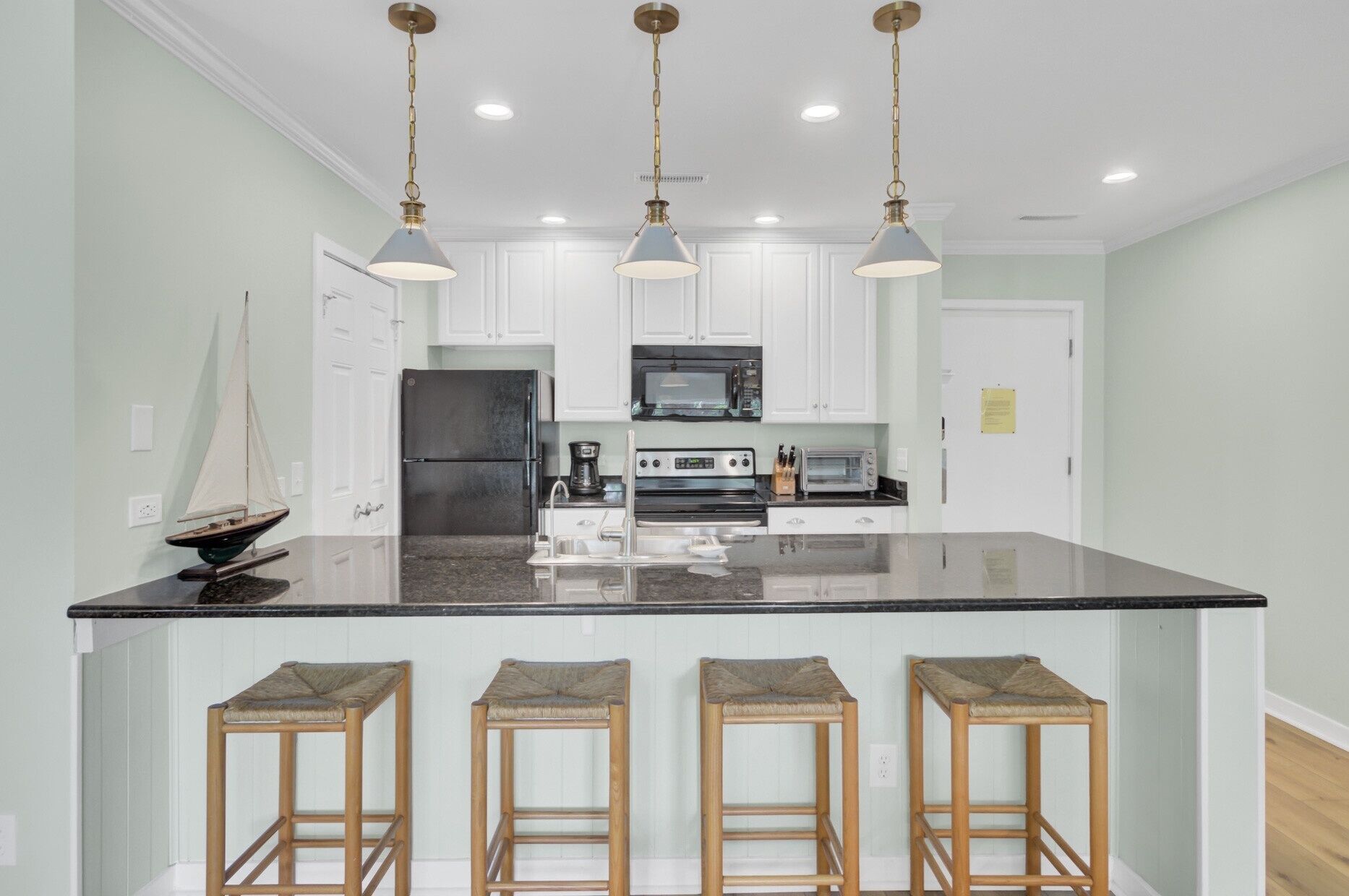 A kitchen with a central island, white cabinets, stainless steel appliances, and three bar stools.
