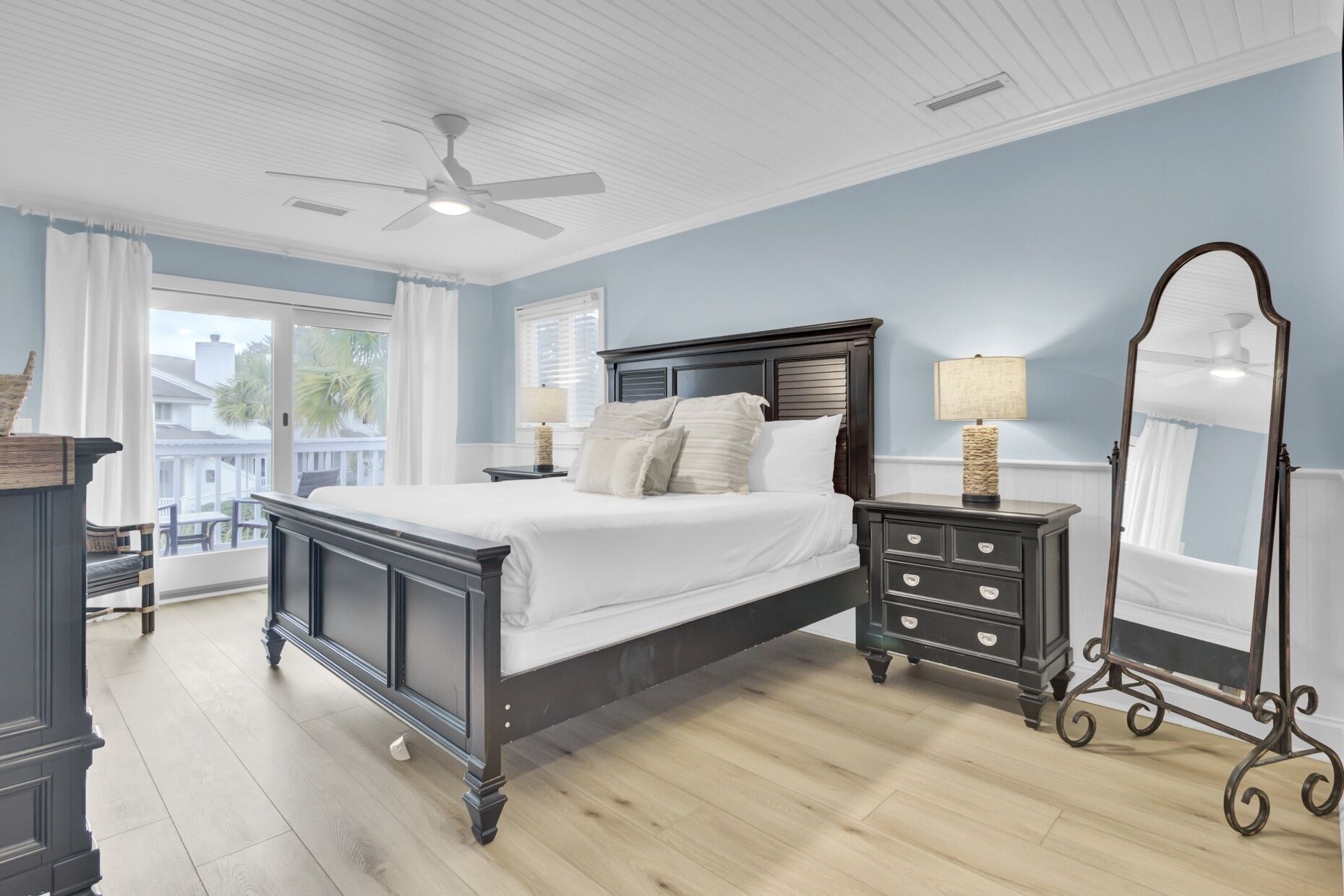 A bedroom with a large bed, a dresser, a mirror, and a ceiling fan.