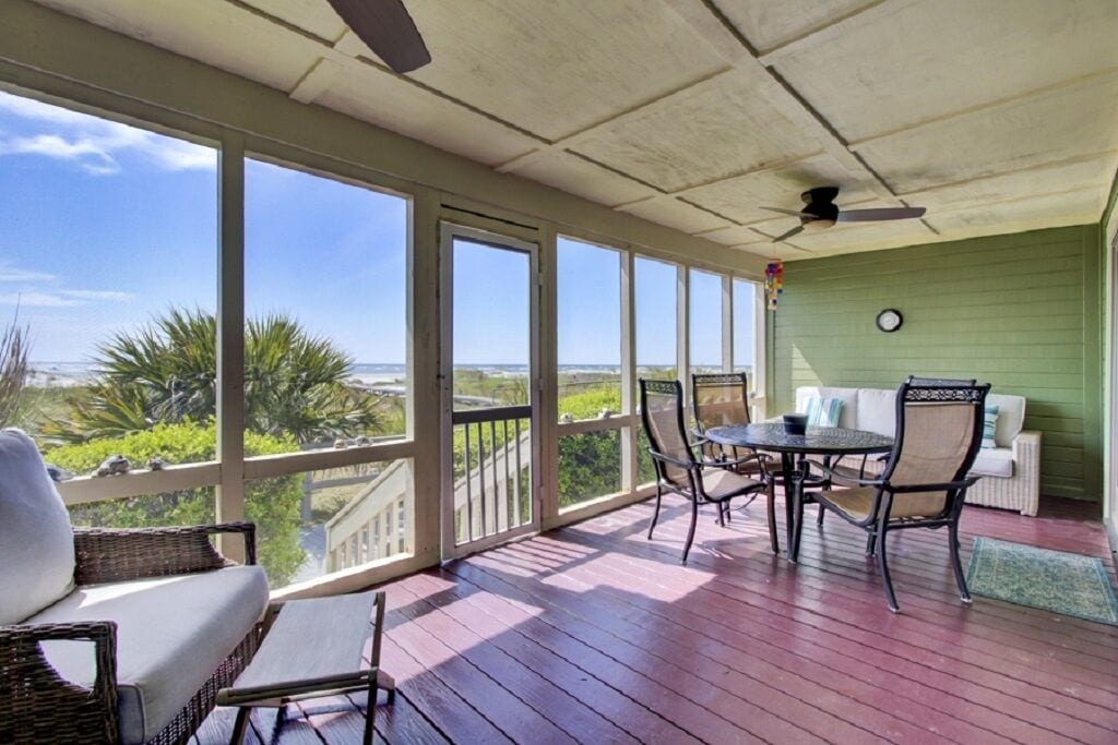 A covered patio with a view of the ocean, wicker furniture, and a green wall with a clock.