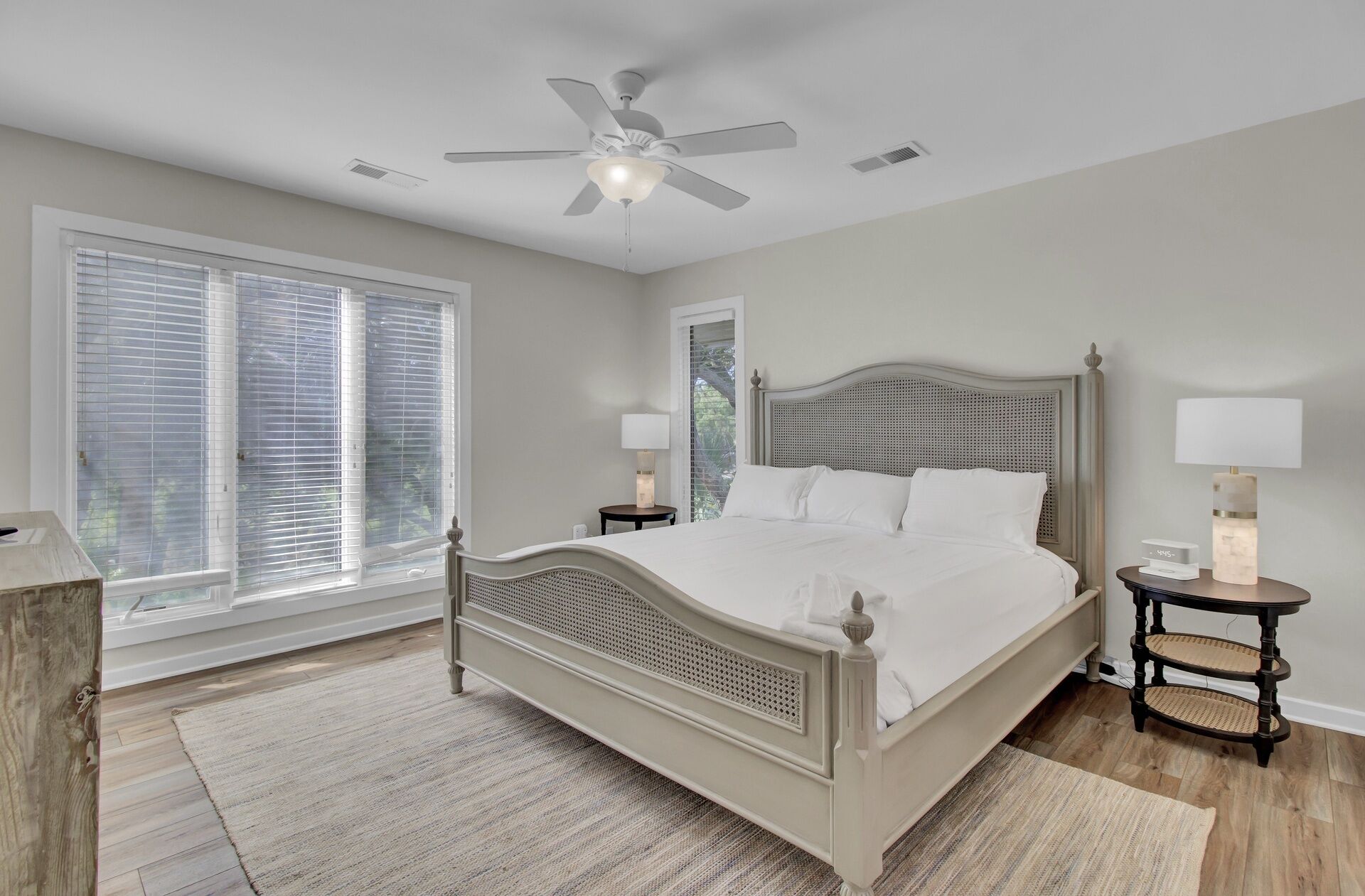 A bedroom with a bed, a ceiling fan, a window with blinds, and a bedside table with a lamp.