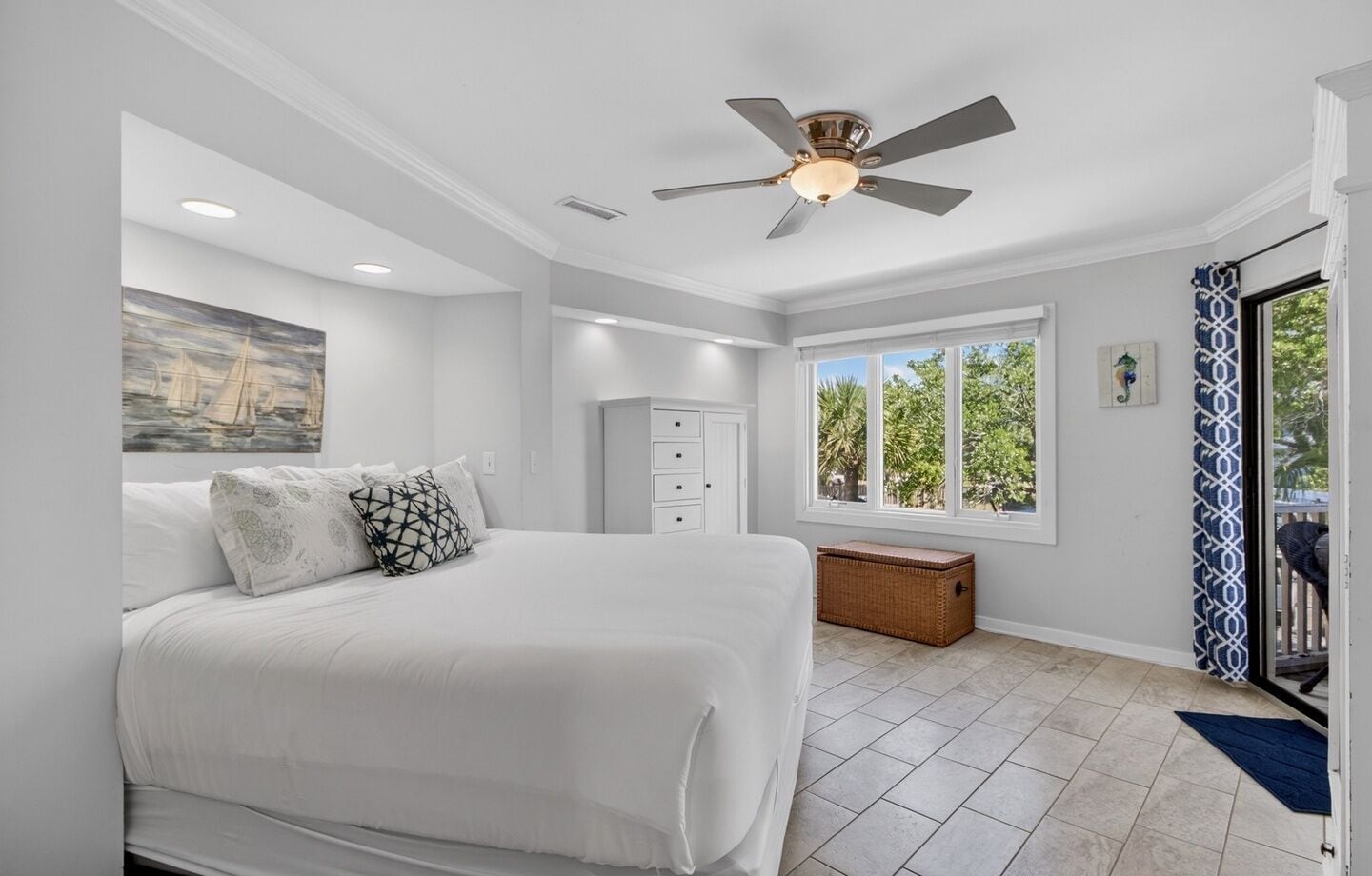 A bedroom with a bed, a ceiling fan, a window, a dresser, and a small chest of drawers.