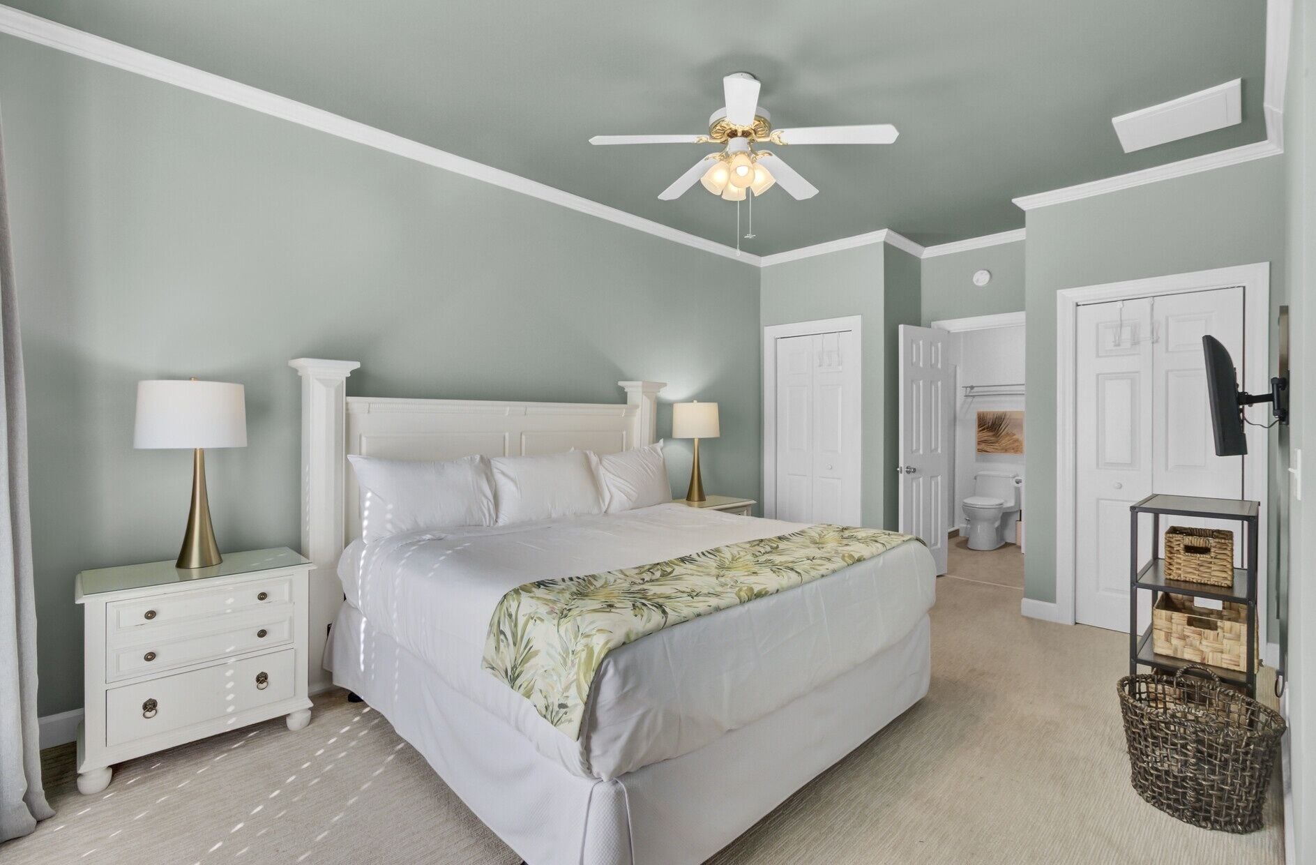 A bedroom with a bed, nightstands, a ceiling fan, a lamp, and a door leading to a bathroom.