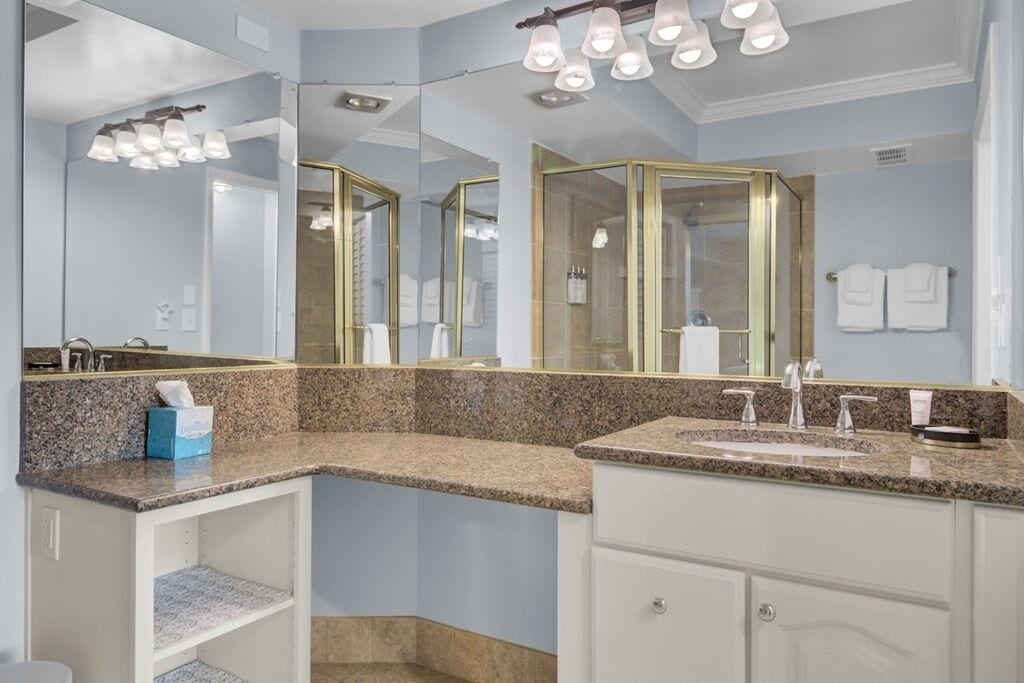 Une salle de bain dotée d’un comptoir en granit, d’un grand miroir avec un cadre doré et d’une douche avec une porte en verre.