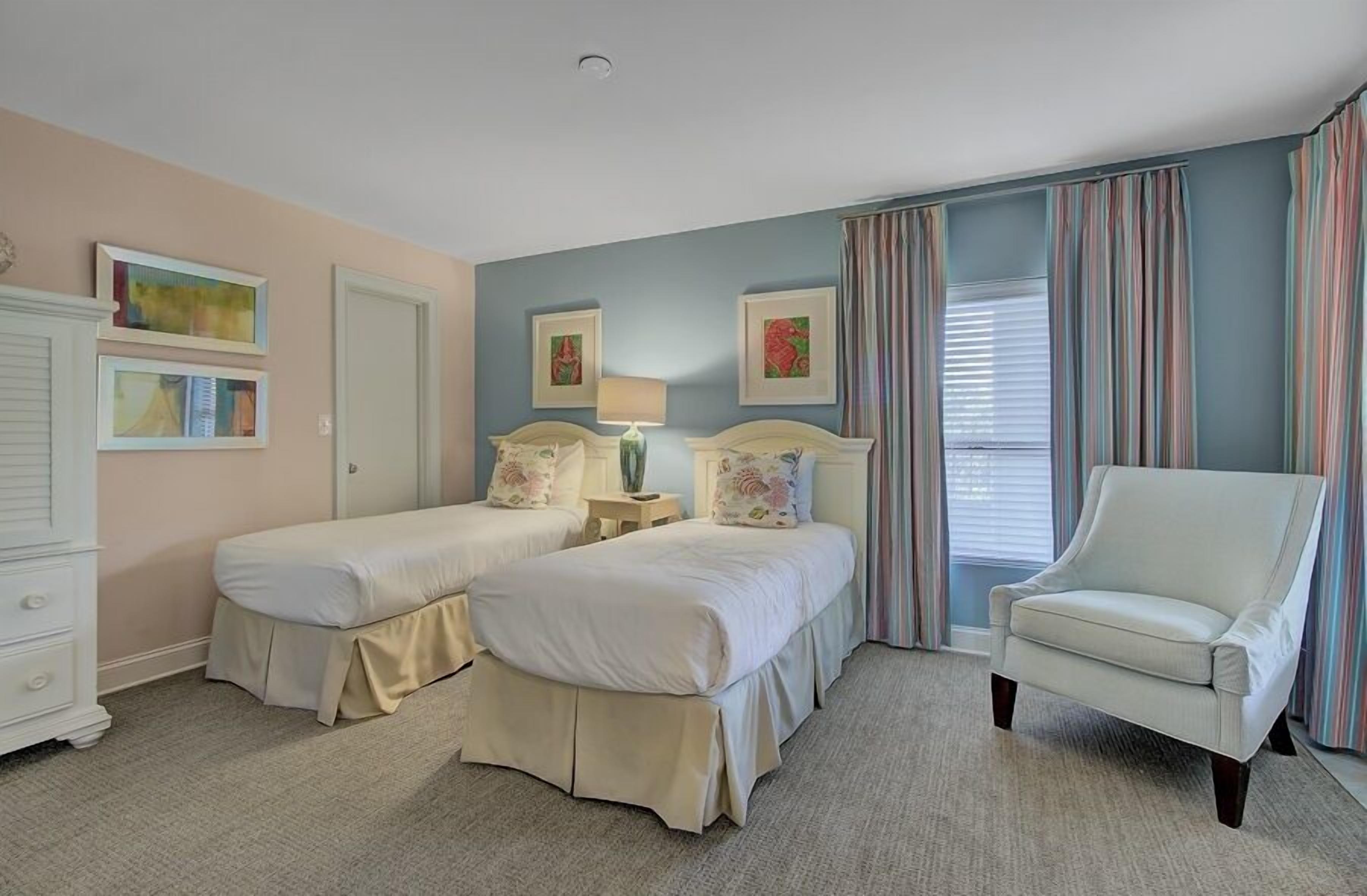 A bedroom with two beds, a chair, and a dresser.