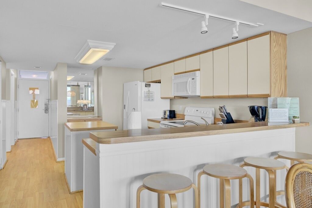 Una cocina moderna con armarios blancos, una isla central con taburetes y un microondas sobre la estufa.