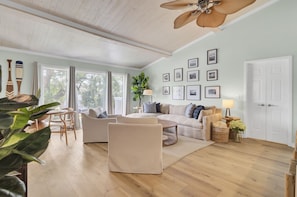 Un salon spacieux doté d’un plafond en bois, de grandes fenêtres, d’un ventilateur de plafond et de différents types de sièges.