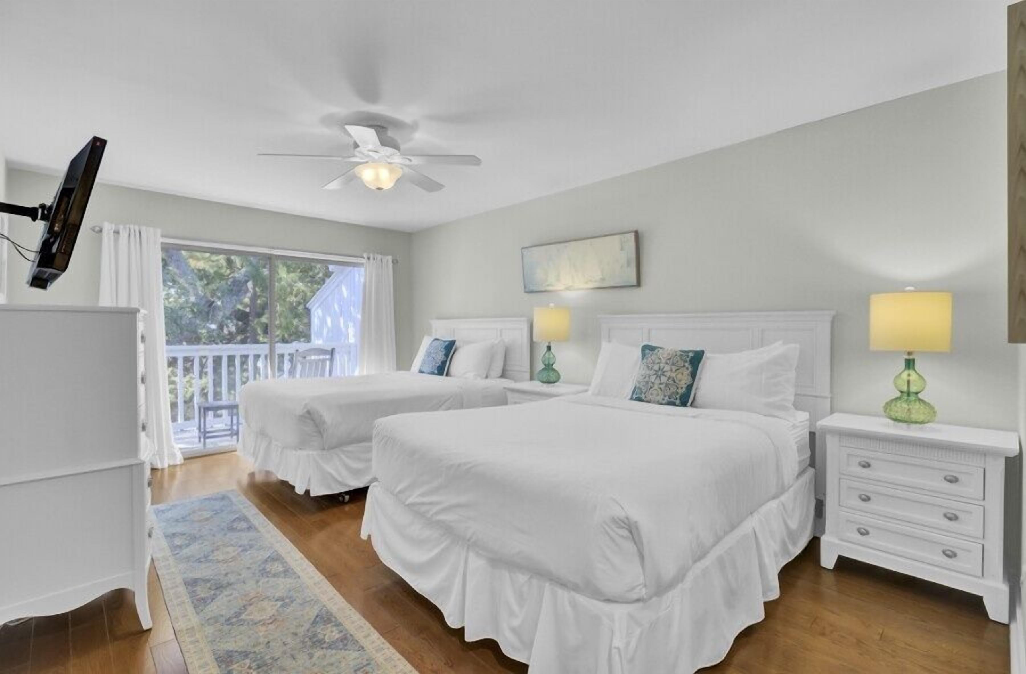 A bedroom with two beds, a ceiling fan, a TV, and a balcony.
