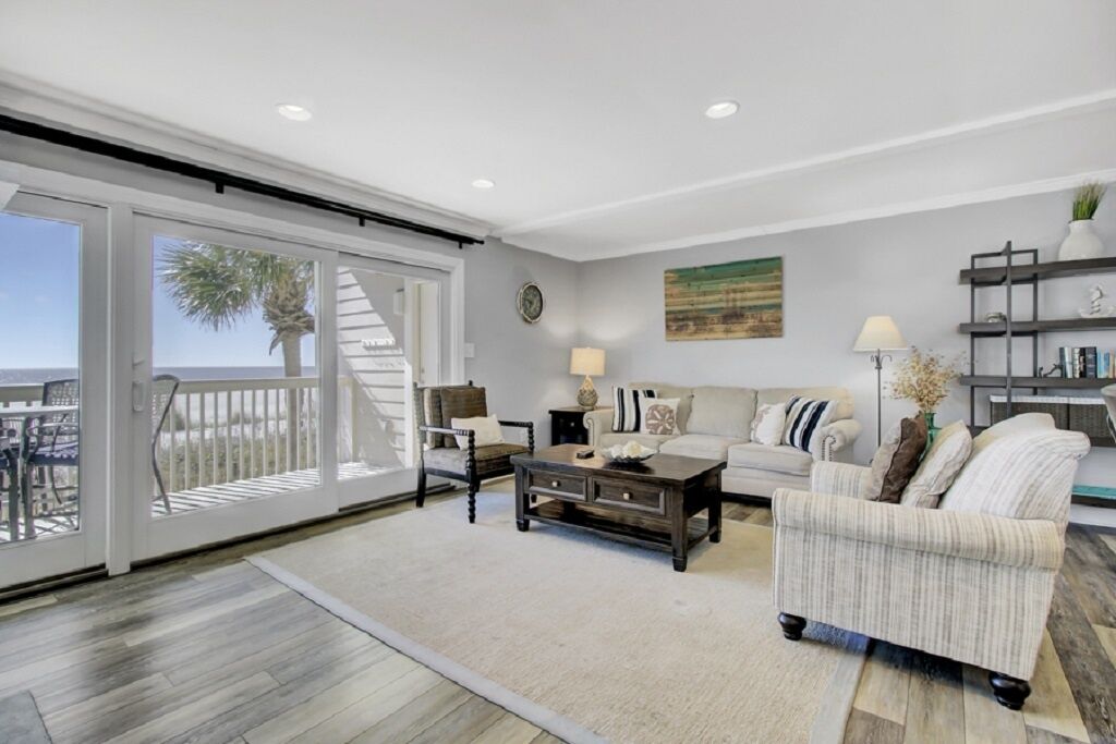 A spacious living room with a large sliding glass door leading to a balcony, a sofa, a coffee table, and a bookshelf.