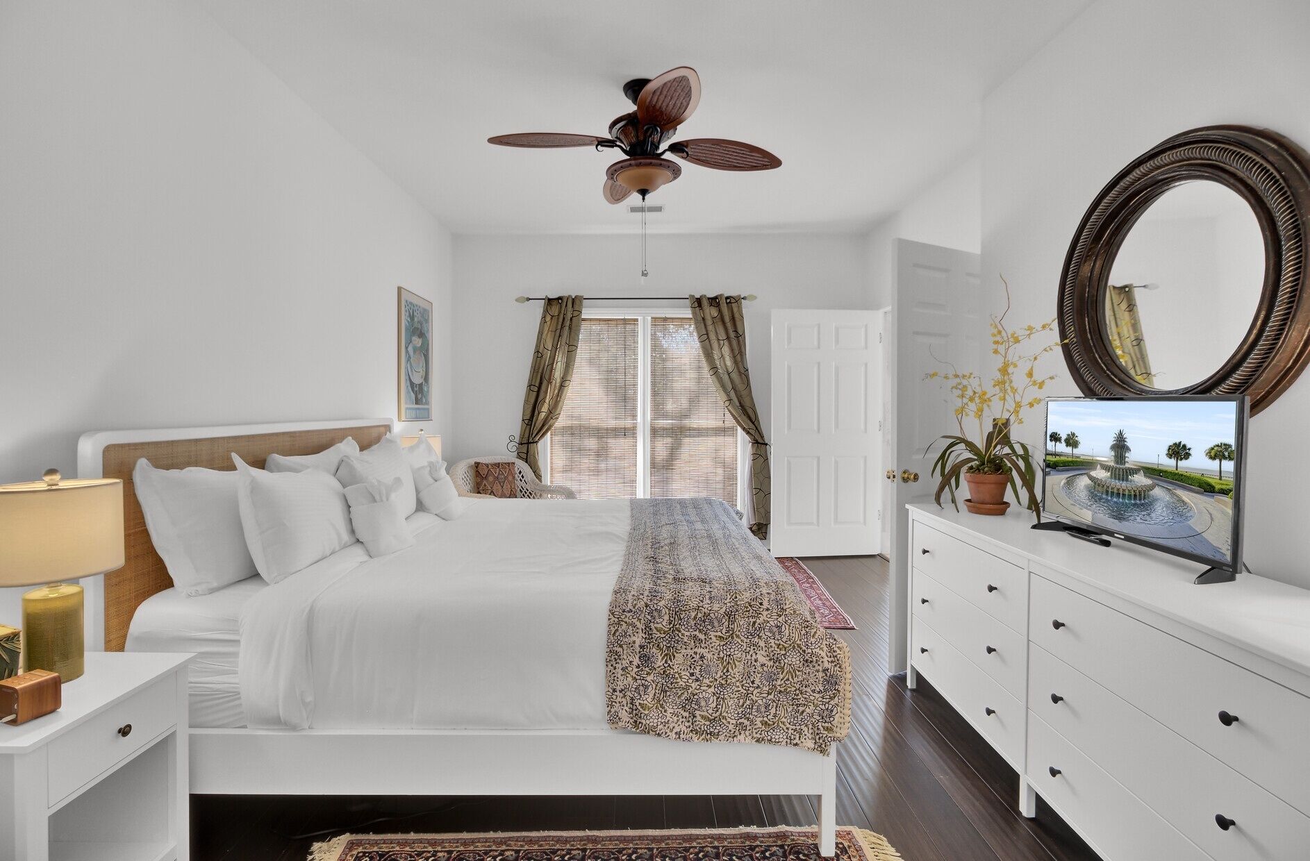 A bedroom with a bed, a ceiling fan, a TV, a dresser, and a window with curtains.