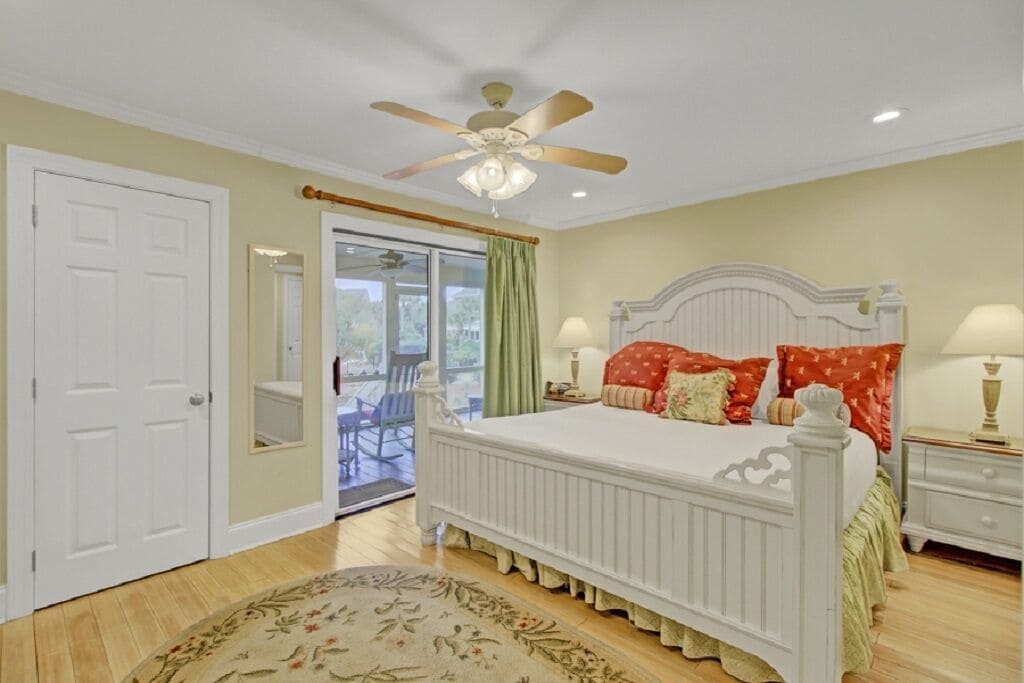 A bedroom with a bed, a ceiling fan, a nightstand, and a view through a glass door to an outdoor area.