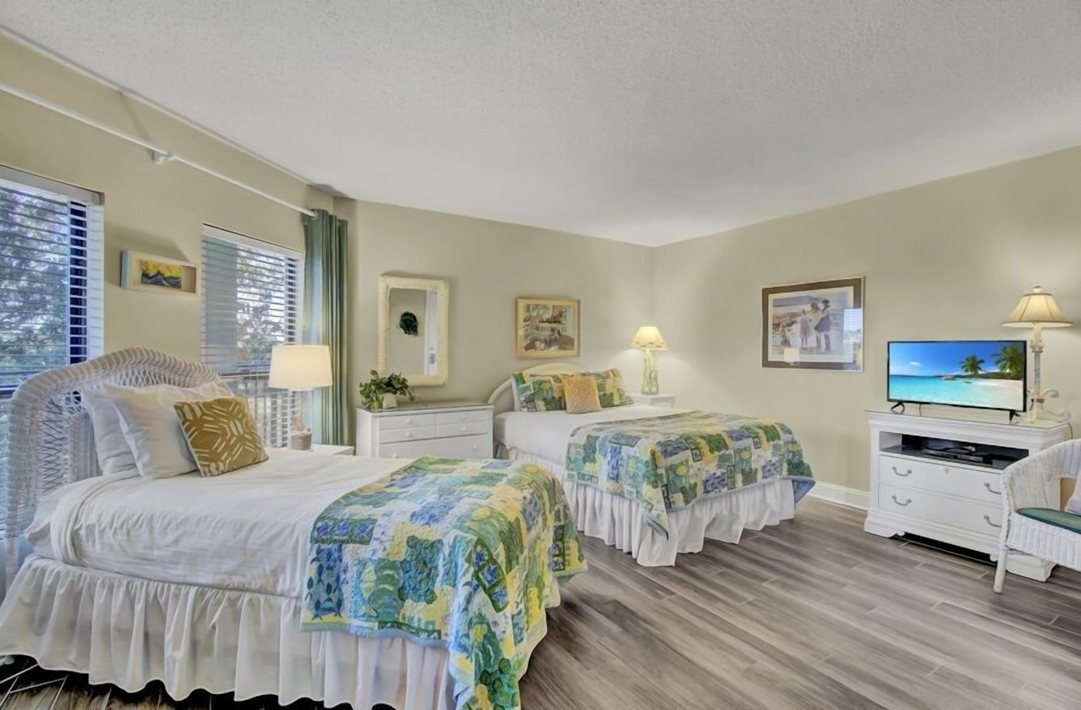 A bedroom with two beds, a TV, and a dresser.