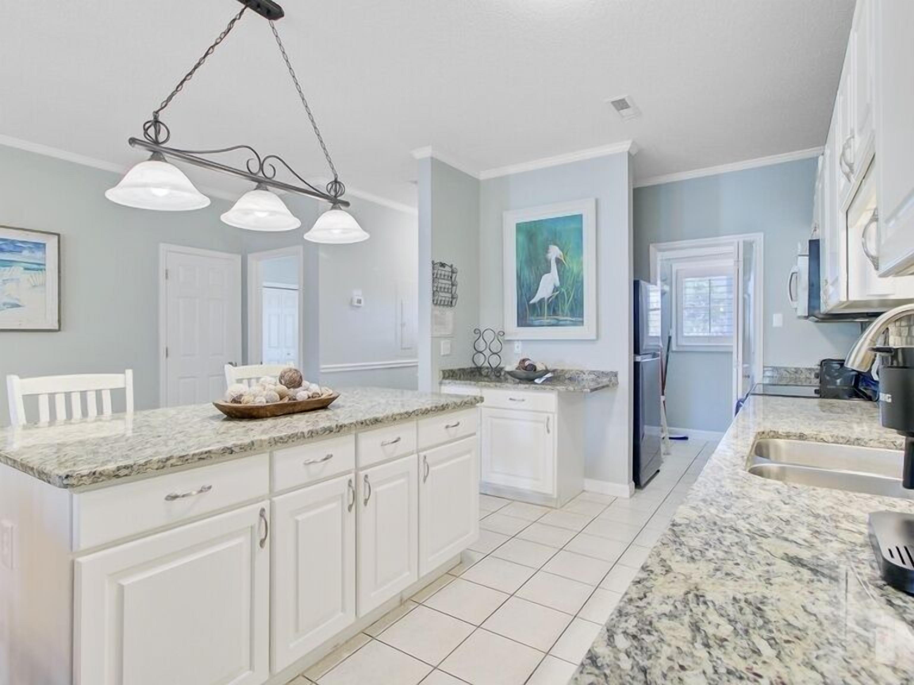 A kitchen with white cabinets, granite countertops, and a hanging light fixture.