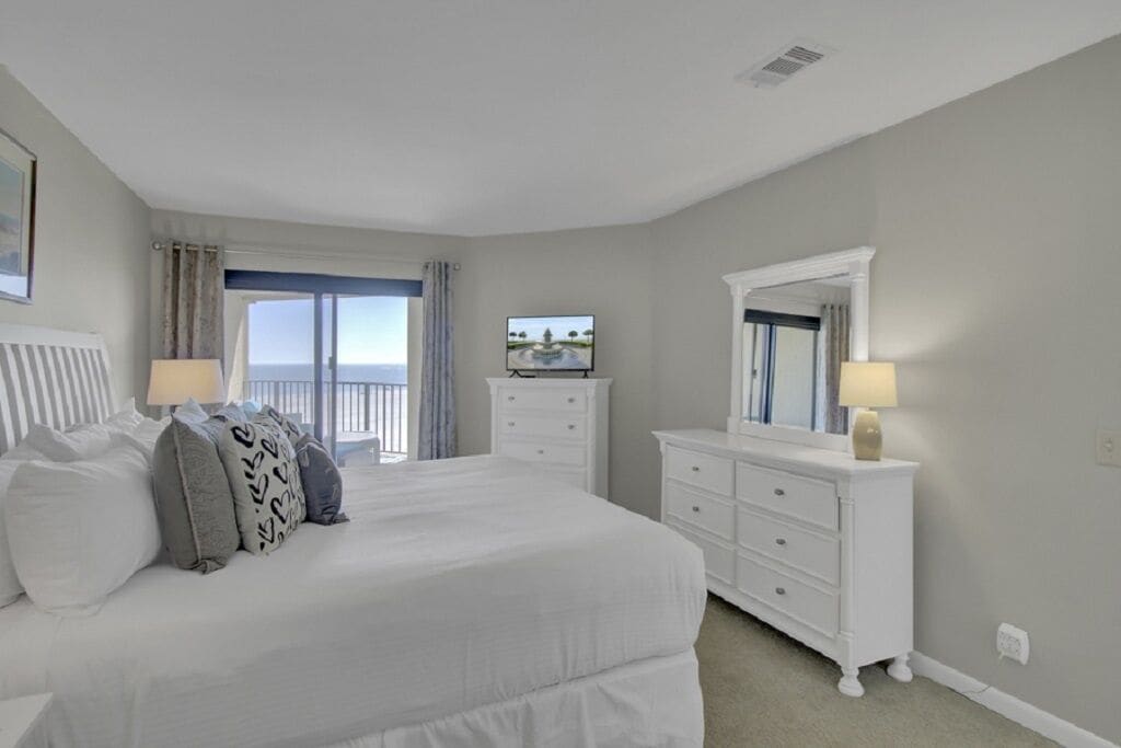 A bedroom with a bed, a dresser, a mirror, a television, and a balcony with curtains.