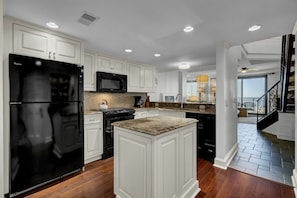 A modern kitchen with white cabinetry, a black refrigerator, a microwave, and a granite countertop island. - Wild Dunes Vacation Condos 3&4 Bedrooms (Isle of Palms)