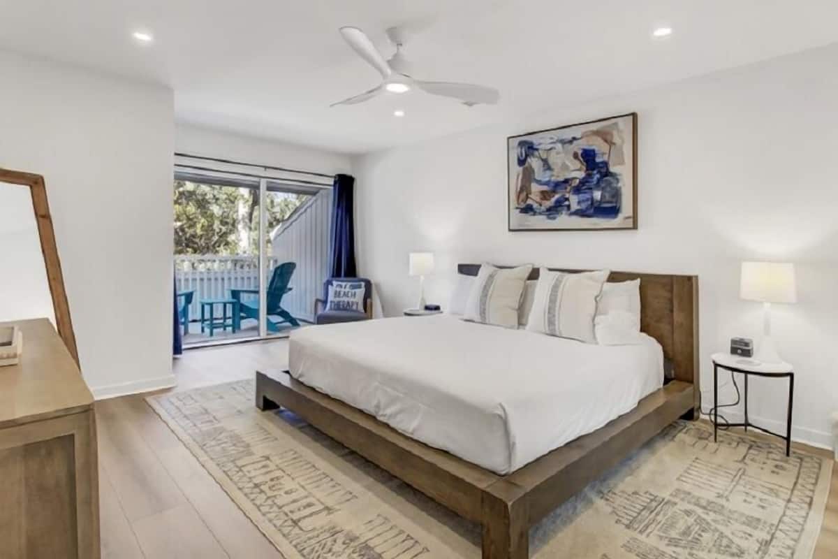Un dormitorio con una cama grande, un ventilador de techo, un cuadro y vistas al exterior.