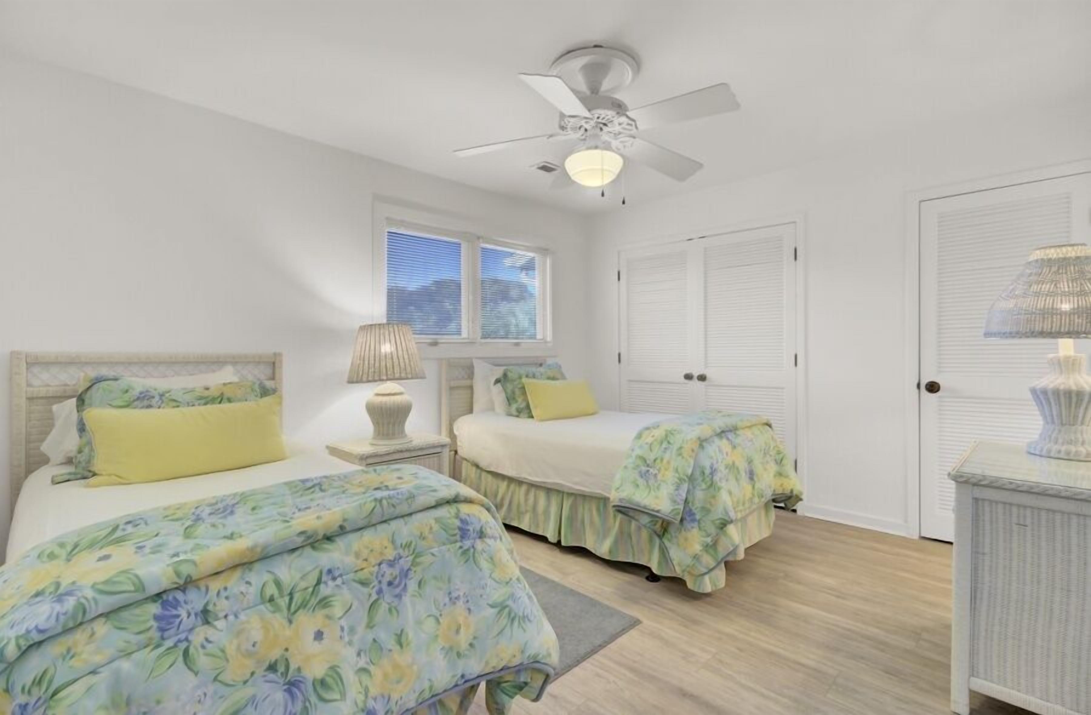 A bedroom with two beds, a ceiling fan, a window, and a door.