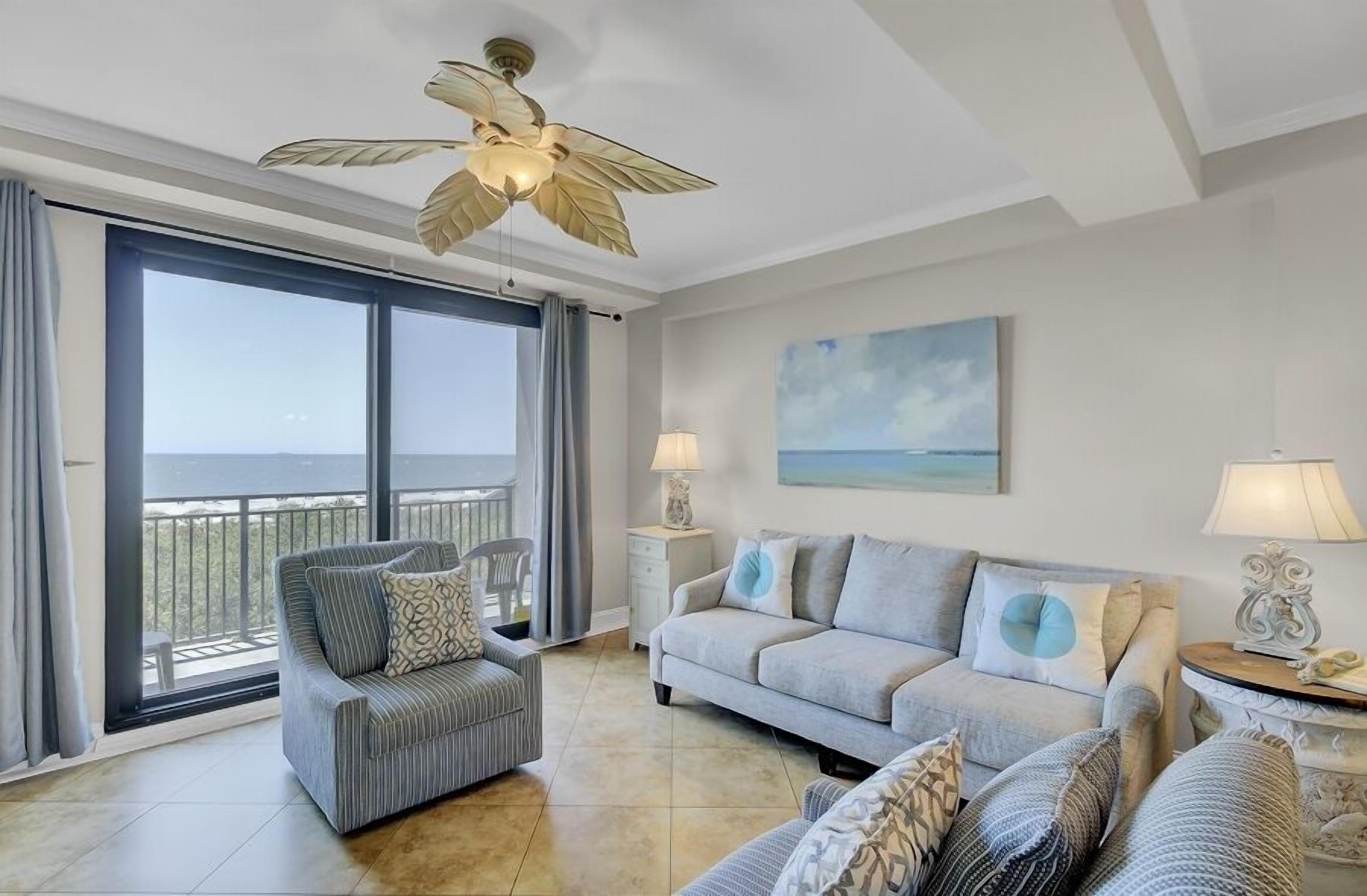 A spacious living room with a balcony, a ceiling fan, and a painting of a beach.