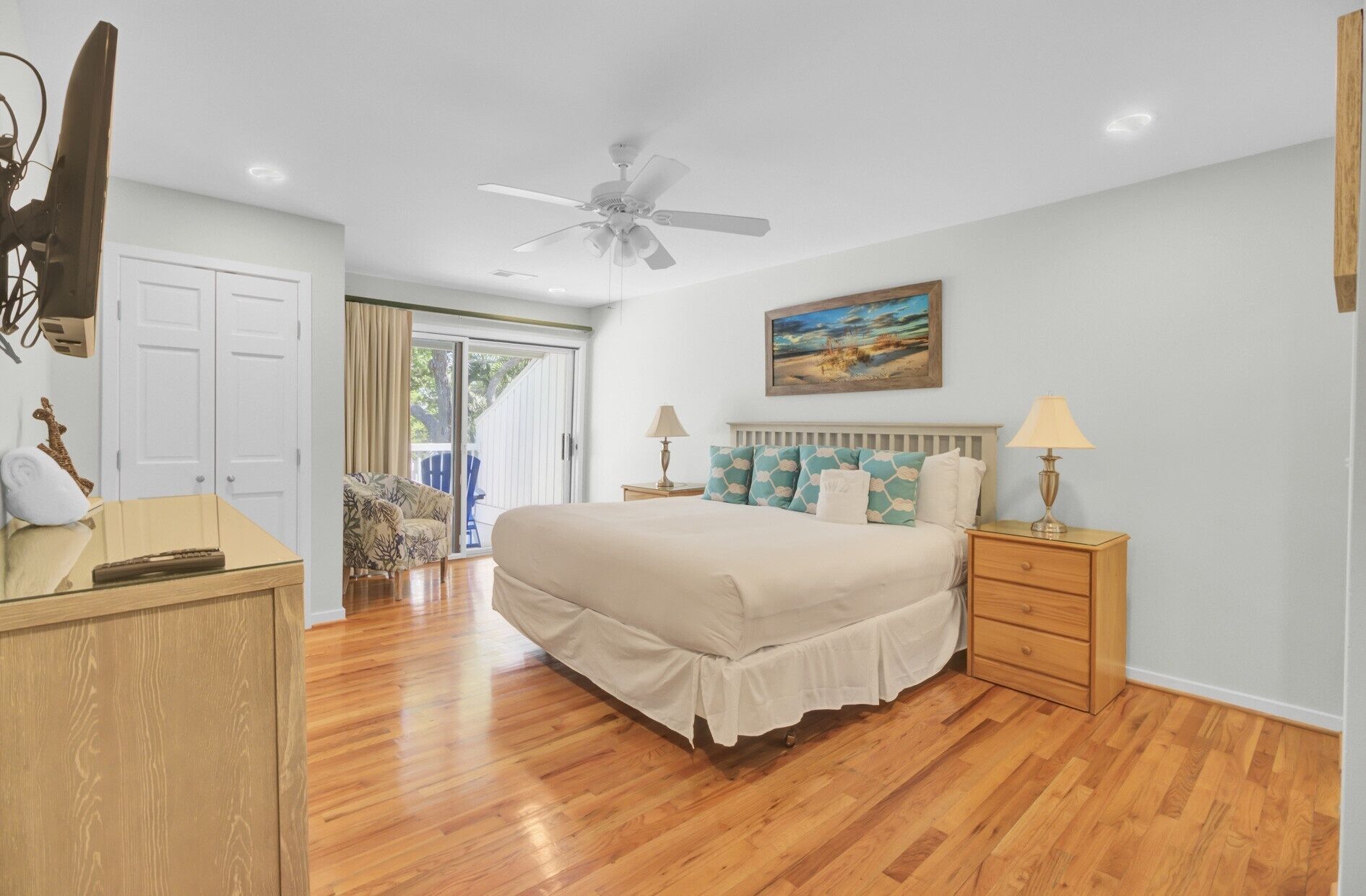 A bedroom with a bed, bedside tables, a ceiling fan, and a painting on the wall.