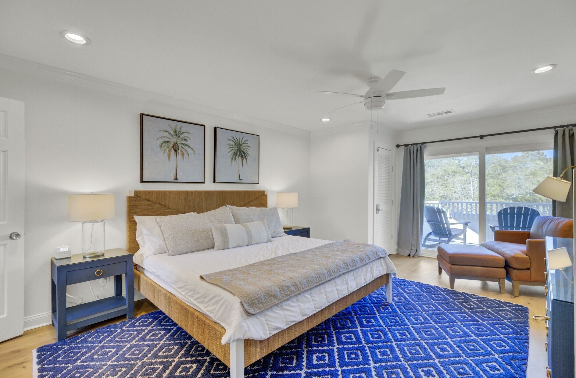 A bedroom with a bed, nightstands, a ceiling fan, and a view to the outside.