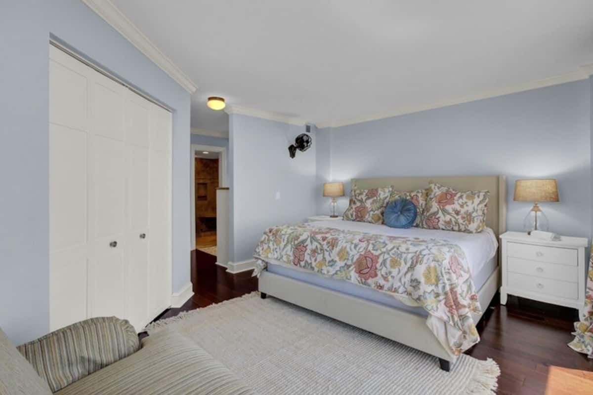 Un dormitorio con cama, mesitas de noche, una puerta y un pasillo.