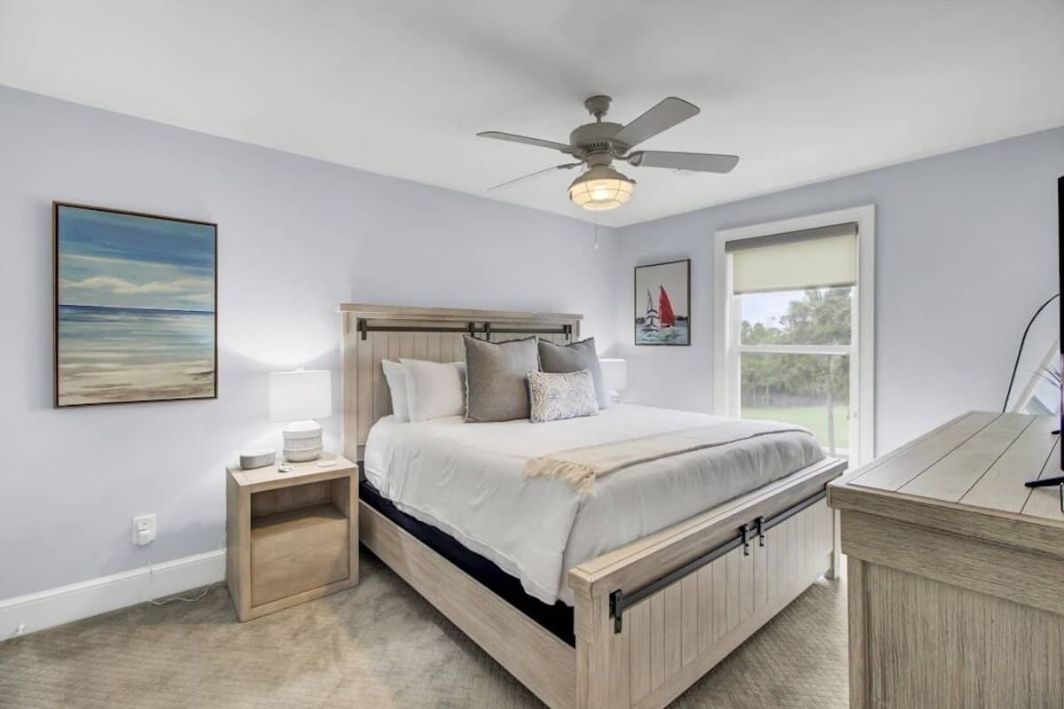 Un dormitorio con cama, mesita de noche, ventilador de techo y ventana con vistas.