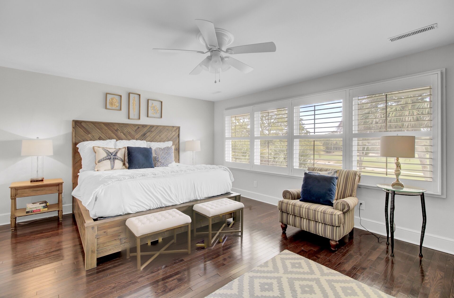 A bedroom with a bed, bedside tables, a chair, a window with blinds, and a ceiling fan.